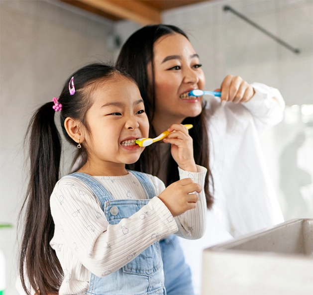 Woman and her young daughter brushing their teeth together