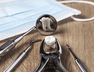 Extracted tooth in forceps next to dental instruments 