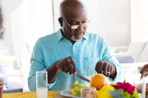 Man in light blue shirt cutting up fruit on his plate at the table